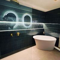 Modern Bathroom with Dark Tile and Freestanding Tub: A stylish bathroom featuring bold dark tiles, a freestanding white bathtub, and brass fixtures, complemented by illuminated oval mirrors for a sophisticated look.