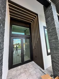 Modern Front Door with Elegant Wooden Slats and LED Accents: A stunning contemporary front door design featuring sleek black glass, textured stone pillars, and illuminated wooden slats creating a dynamic architectural statement.