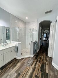 Bright Modern Bathroom with Subway Tile and Wood-Look Flooring: A contemporary bathroom with white subway tile walls, a glass-enclosed shower featuring pebble flooring, and rustic wood-look tile for a clean, stylish aesthetic.