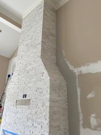 Tall white stone fireplace under construction, showcasing stacked stone tiles and intricate crown molding details.