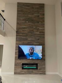 Contemporary fireplace design featuring gray stacked stone, a recessed TV mount, and a vibrant electric fireplace for modern decor.