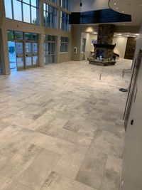 Spacious Living Room with Stone Fireplace and High Ceilings: A grand living room featuring a large stone fireplace, tall windows letting in natural light, and light-toned tile flooring, perfect for a cozy and modern gathering space.