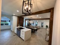 Modern farmhouse kitchen featuring a stylish chandelier, exposed wooden beams, and a spacious open layout with elegant white cabinetry and a marble island centerpiece.