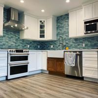 Open kitchen layout with modern white cabinetry, blue mosaic backsplash, and a functional rolling island cart for added versatility and style.