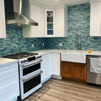 Bright, modern kitchen showcasing a spacious white island with gold-accented handles, minimalist open shelving, and a stainless-steel refrigerator blending with the clean, open-concept living space.