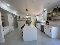 Sleek kitchen interior with white cabinets, a double oven range, and a captivating mosaic tile backsplash in shades of blue, paired with a farmhouse-style sink and light wood flooring for a coastal-inspired vibe.