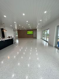 Expansive open-concept living space with polished terrazzo flooring, wood-accented paneling, and a central wall-mounted TV for a clean and minimalist aesthetic.